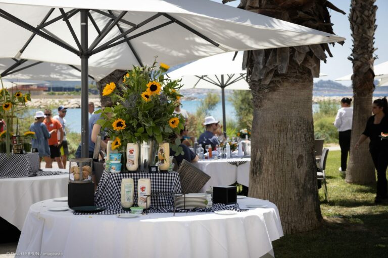 Cocktail evenement corporate BEL France 2022 en bord de mer, mange-debout vichy et bouquets tournesols sous parasols blancs
