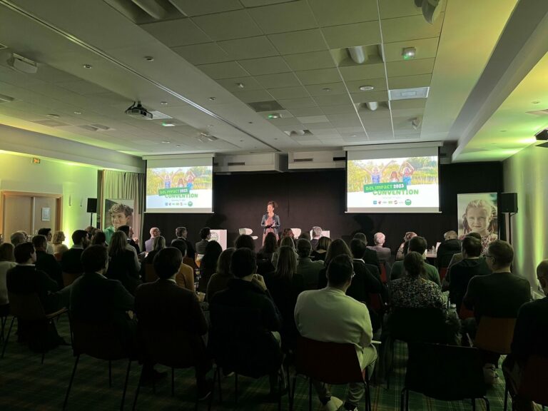 Plenière convention BEL Impact 2023, intervenante sur scène et participants face aux écrans de projection