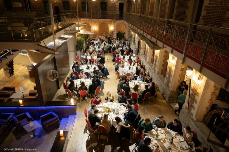 Vue plongeante d'un diner de gala GM 2023 dans une cour interieure patrimoniale, longues tablees et convives reunis.