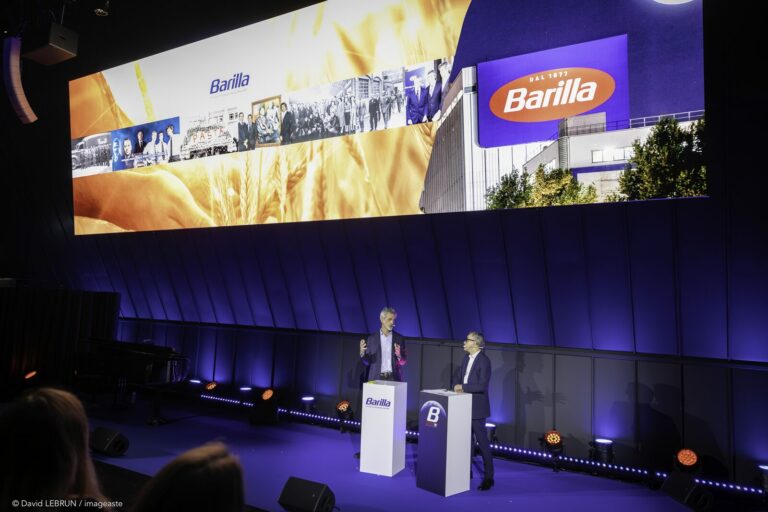 Plénière convention Barilla 2025, deux intervenants sur scène avec pupitres et écran LED panoramique aux couleurs de la marque.