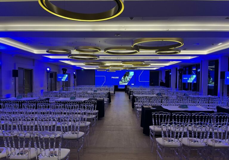 Plénière convention REXEL 2025, salle en ambiance bleue, chaises Napoléon et écrans LED, scénographie corporate